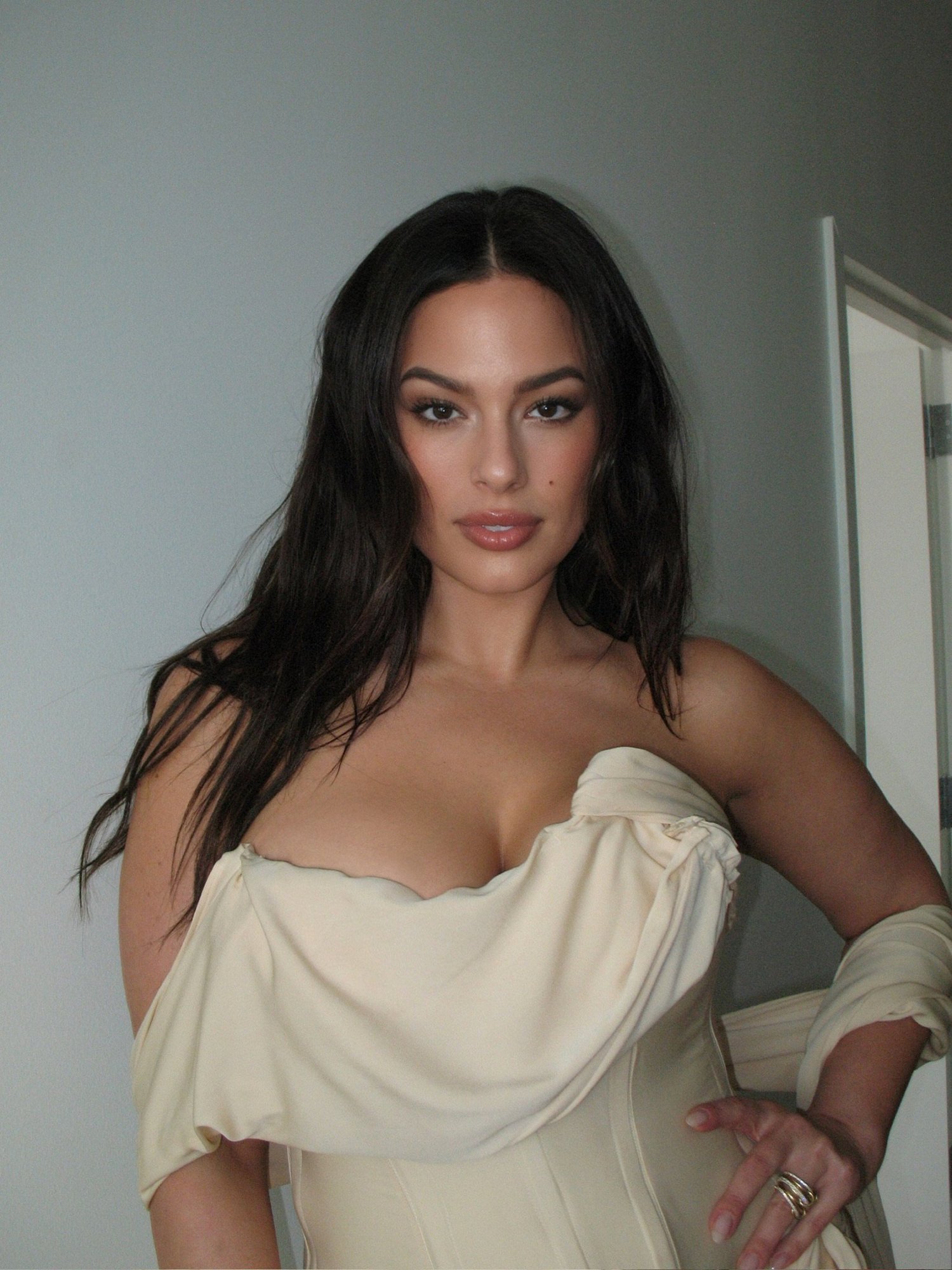 Ashley Graham in a draped ivory corset gown, long dark center-parted waves