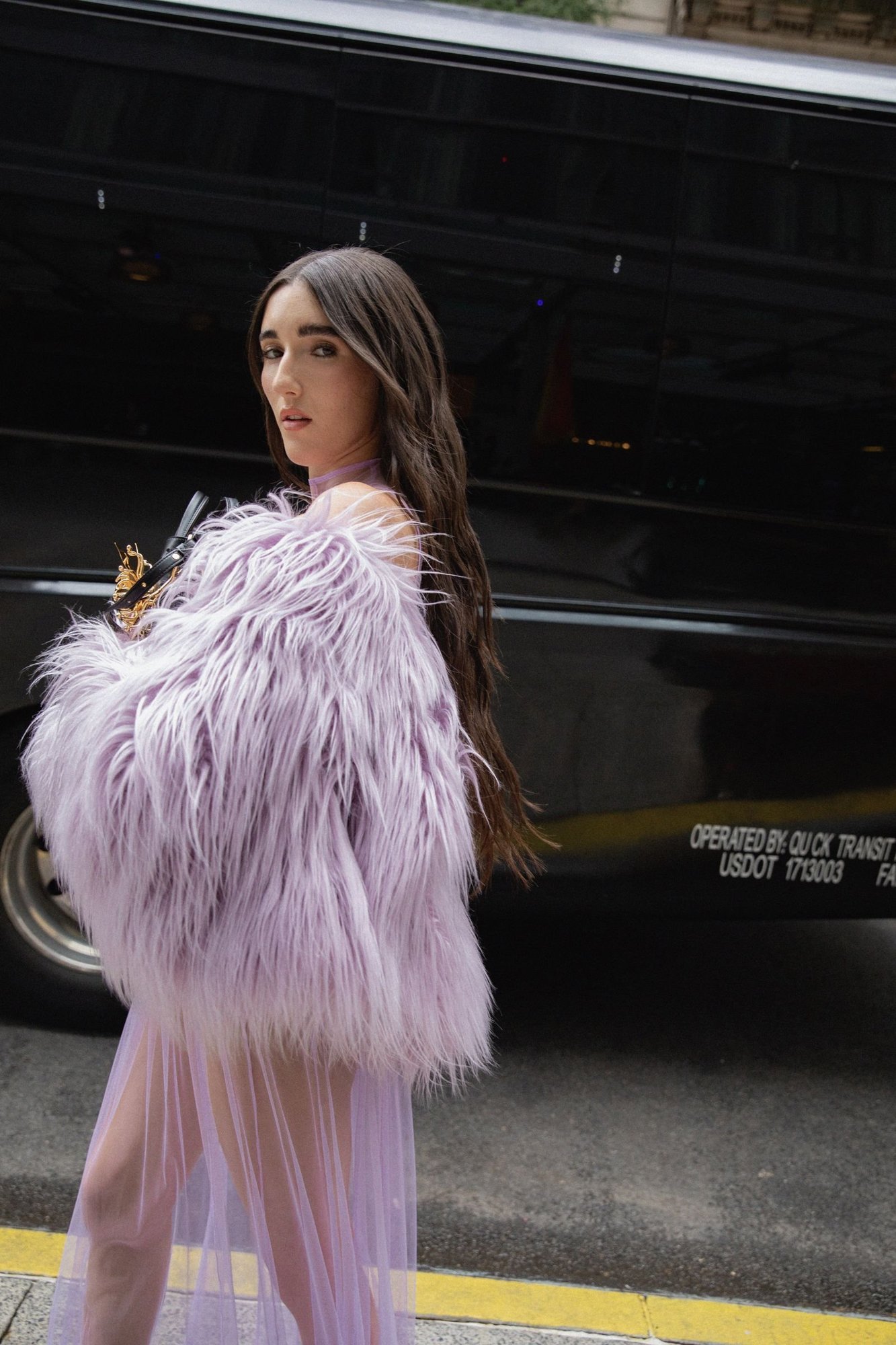 Judeline looking over her shoulder in a lilac faux-fur jacket, long dark waves