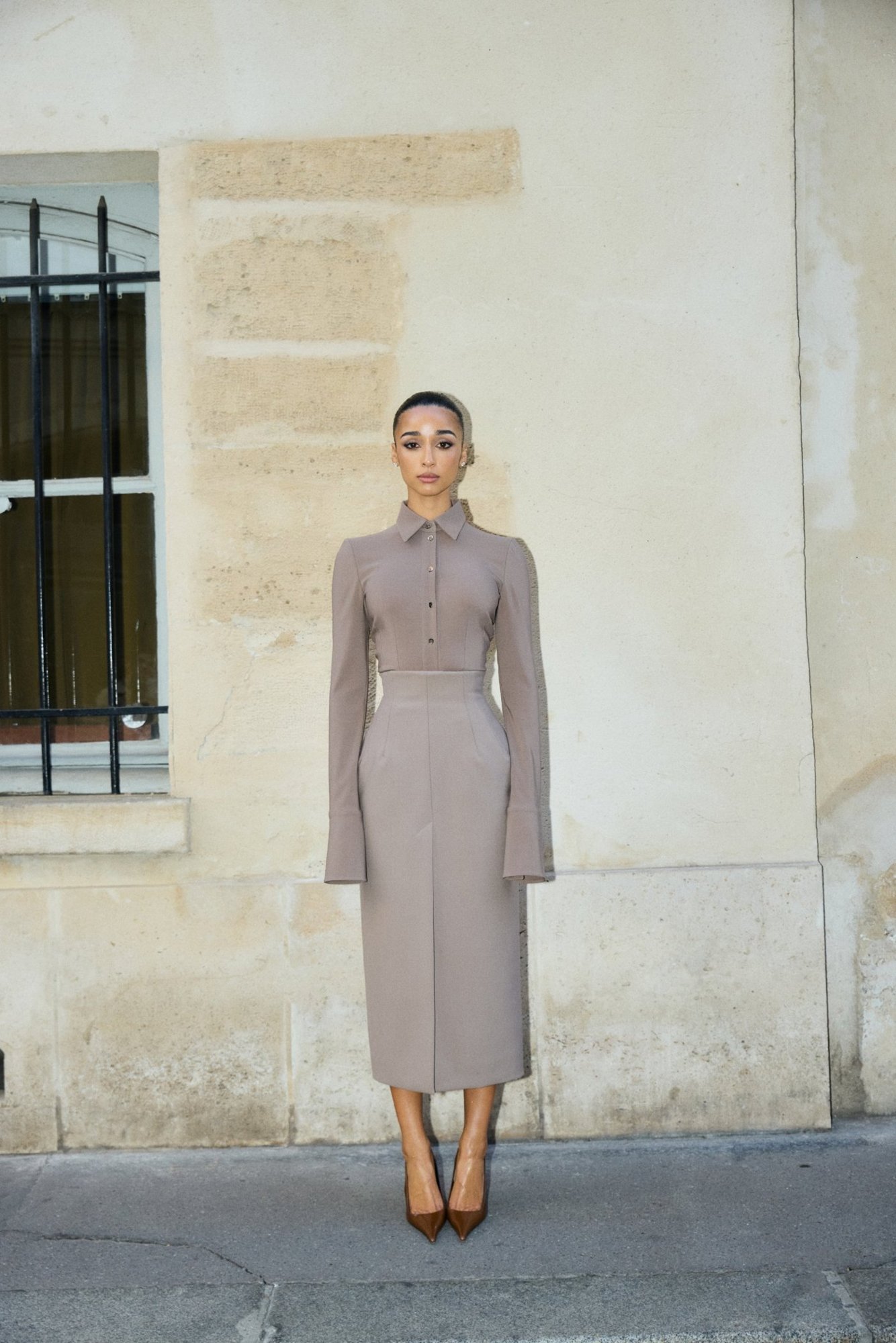 Eloise Dufka standing against a Paris stone wall in taupe Mugler, hair slicked back
