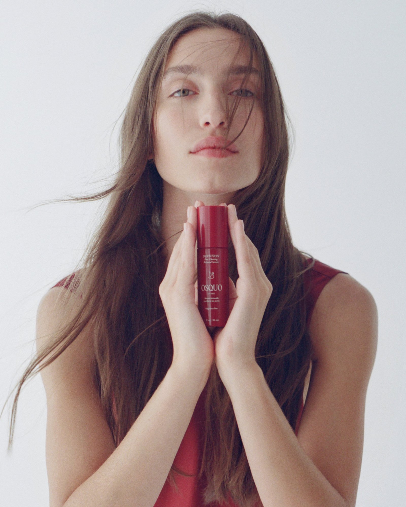 Holding the Devotion serum beneath her chin, long hair blowing across her face