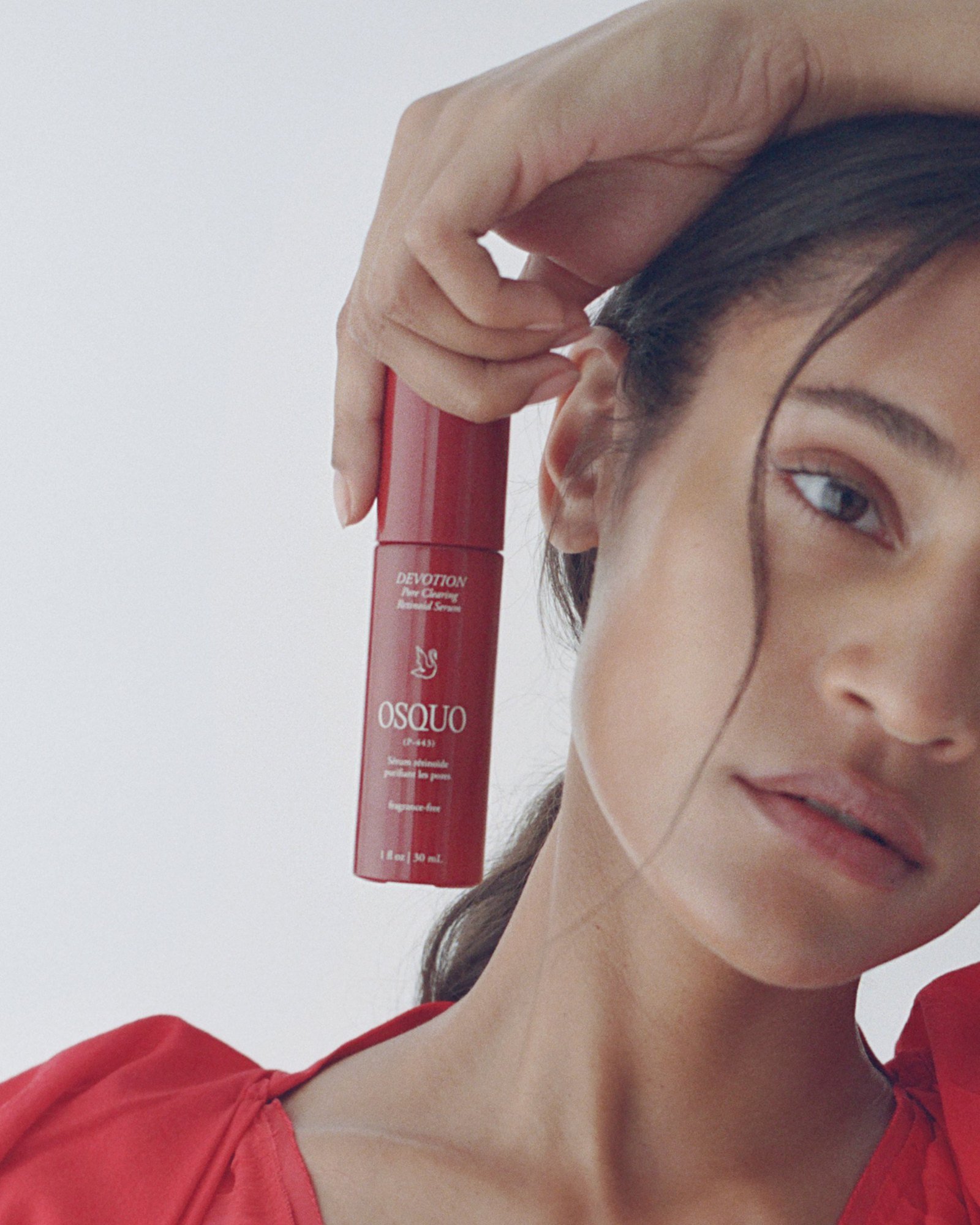 Serum held up by her ear, sleek pulled-back hair with a loose face-framing strand