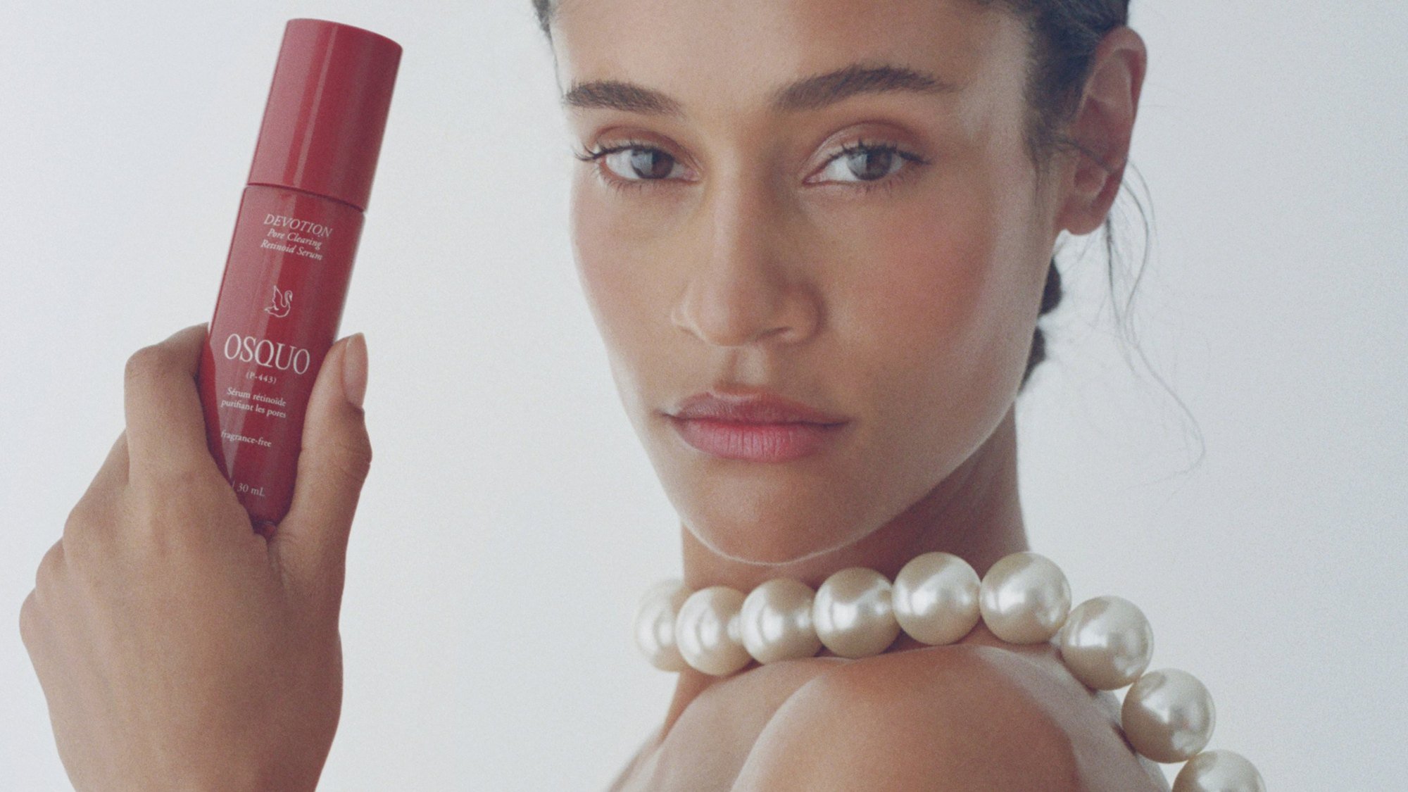 Pearls over her shoulder beside the red Devotion serum, hair pulled back