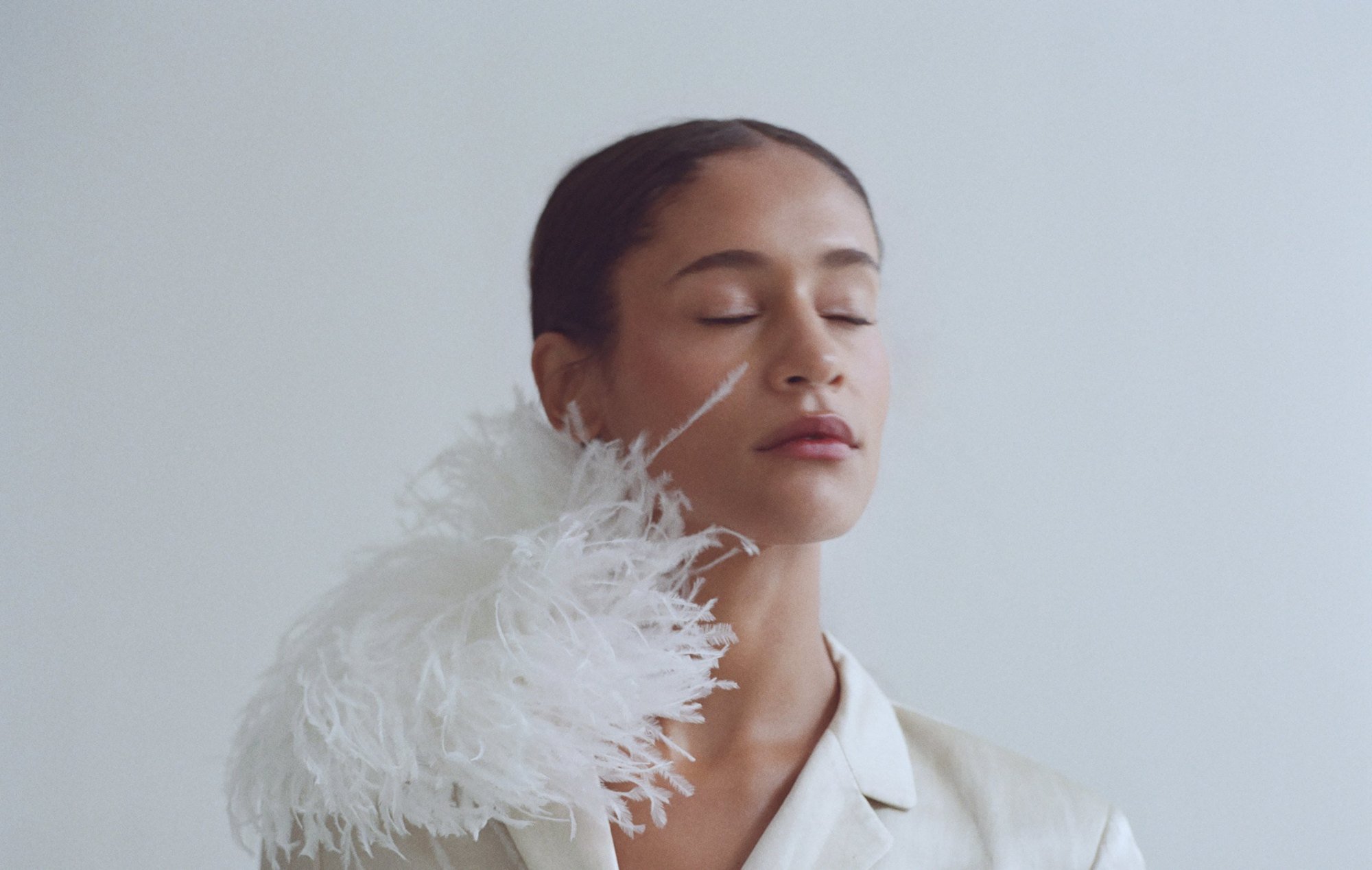 Eyes closed in a white feather collar, hair in a sleek low bun