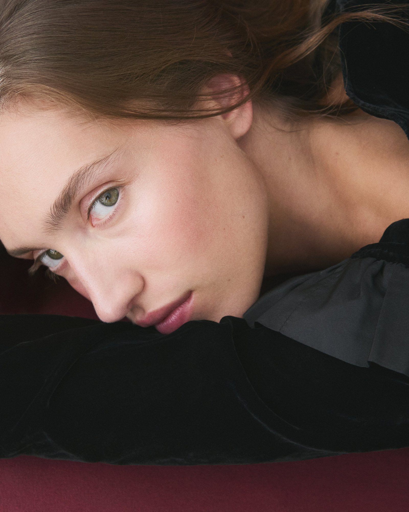 Close-up resting on black velvet, soft pulled-back hair with loose pieces