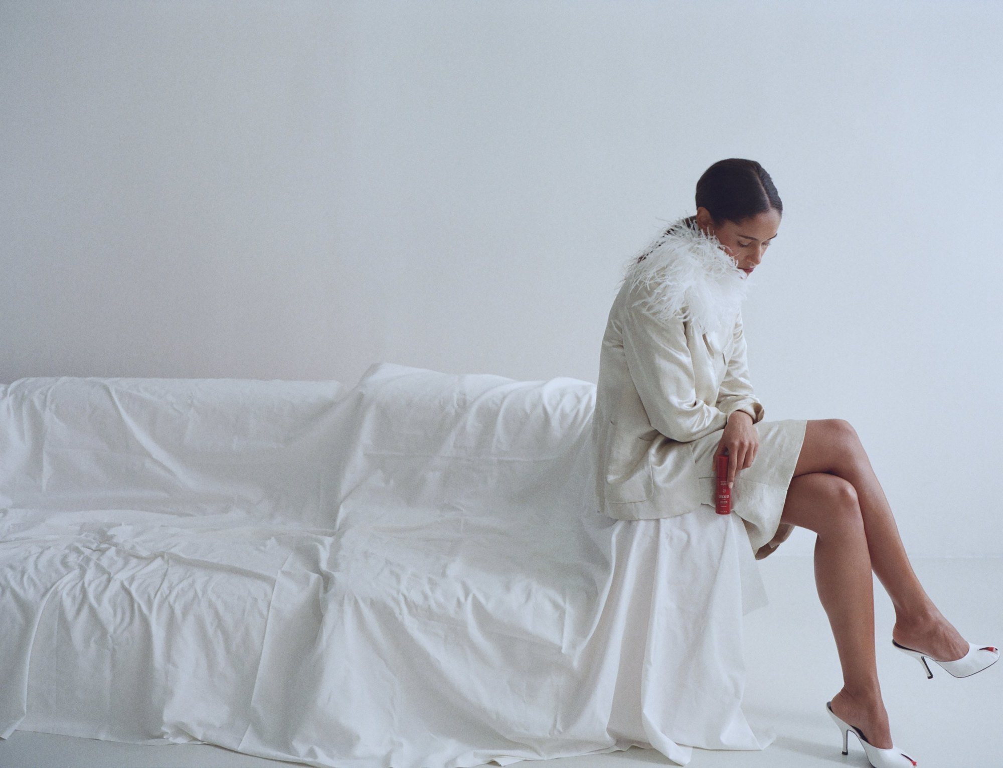 Seated on a white sofa in a feather coat, low bun in profile