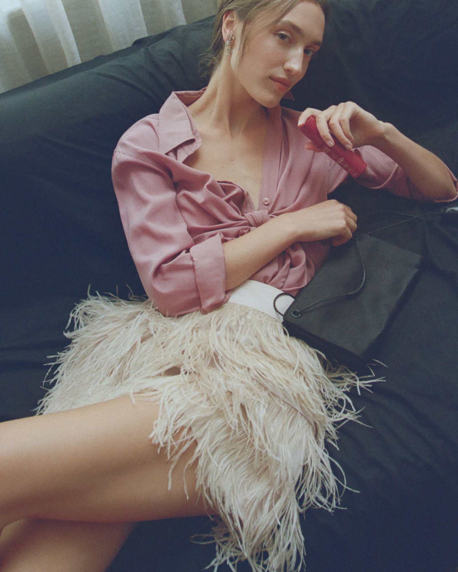 Pink shirt and feather skirt on a black sofa, hair pulled back with soft pieces