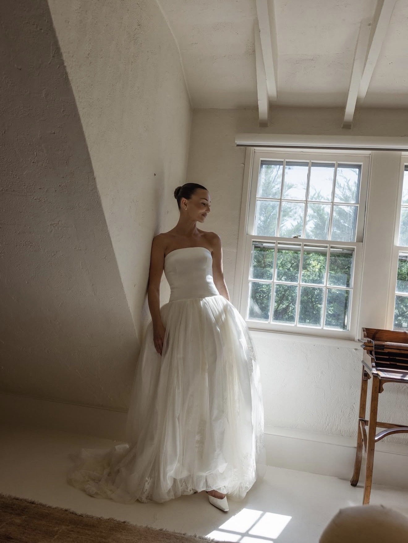Sarah Hill in a strapless gown by an attic window, hair in a sleek low bun