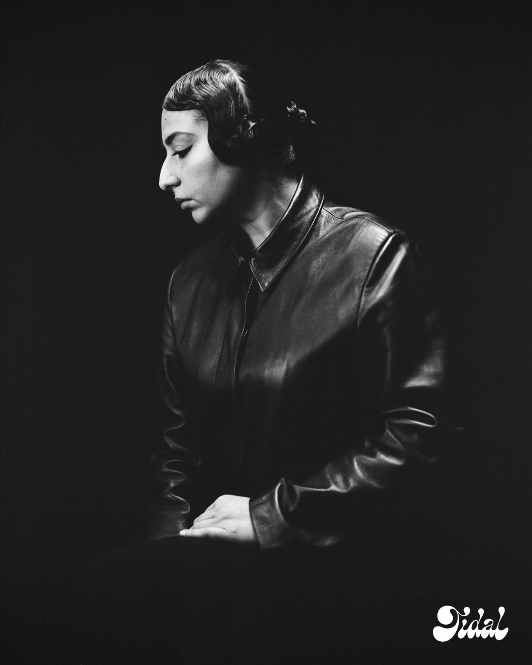 Black and white portrait of Arooj Aftab in a leather jacket, hair sculpted into sleek finger waves and a low knot