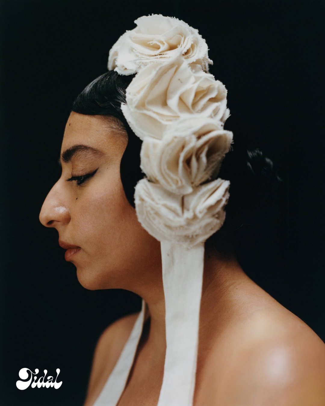Arooj Aftab in profile wearing a sculptural cream fabric rose headpiece over sleek dark hair